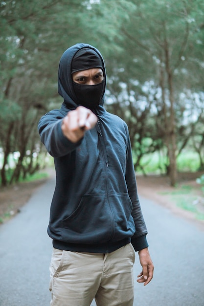 Villain in a mask with a knife wearing black hoodie pointed the knife when stand on the road