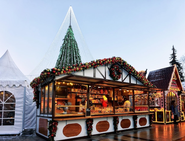 Vilnius, Lithuania - December 3, 2016: Christmas tree with decorations and gingerbread souvenir houses with people  at Xmas market on Cathedral Square, Vilnius. Tree has fairy lights as bridal veiling