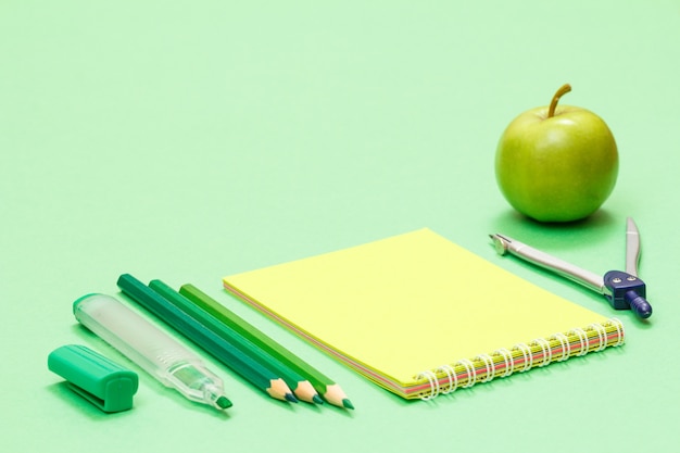 Viltstift, kleurpotloden, notitieboekje, kompas en appel op groene achtergrond. Terug naar schoolconcept. Schoolspullen. Ondiepe scherptediepte.
