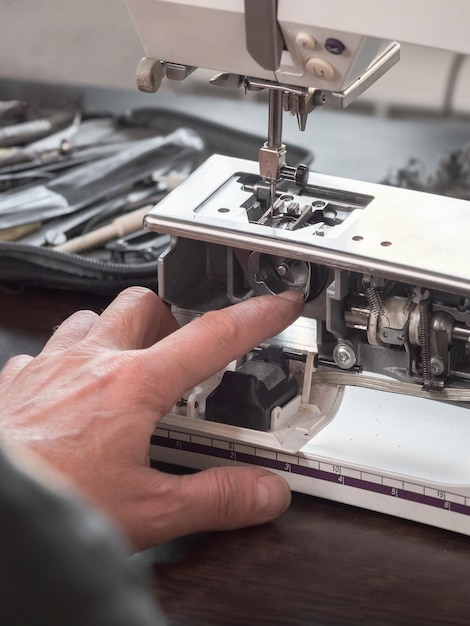 Vinger van de naaimachine-afsteller repareert het interne mechanisme Professionele afstelling van een naaimachine in een kleine fabriek Reiniging en reparatie van professionele apparatuur Verticaal zicht