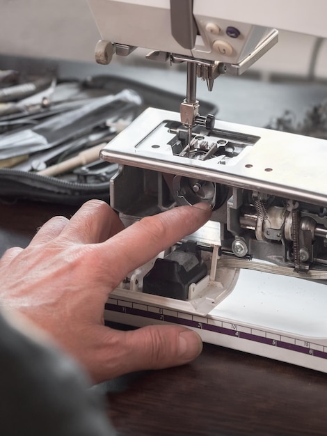 Vinger van de naaimachine-afsteller repareert het interne mechanisme professionele afstelling van een naaimachine in een kleine fabriek reiniging en reparatie van professionele apparatuur verticaal zicht