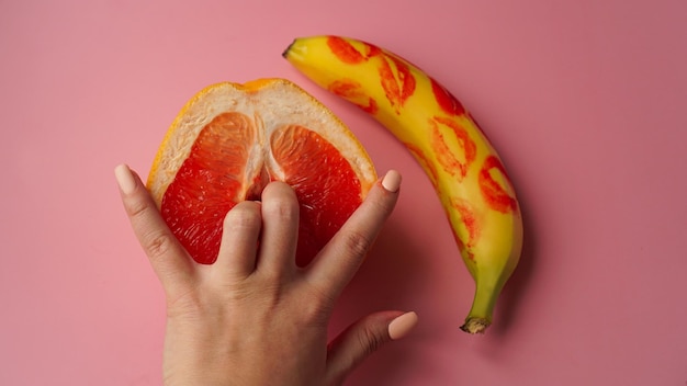 Vingers in grapefruit op roze achtergrond. Samenstelling met verse banaan met sporen van rode lippenstift en grapefruit op roze achtergrond.