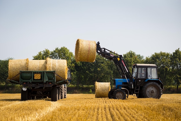 VinnitsaUkraine July 262016huge tractor collecting haystack in the field at nice blue sunny dayTractor collecting straw balesAgricultural machine collecting bales of hayharvest concept