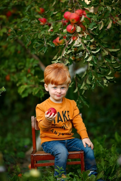 Vinnytsia, Oekraïne, 15 september 2022 Een roodharig jongetje in een appelboomgaard eet een rode appel