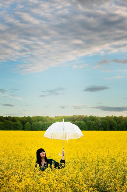 Vinnytsia Ukraine May 15 2022 A girl with black hair and a green dress holds a transparent umbrella in a rape field