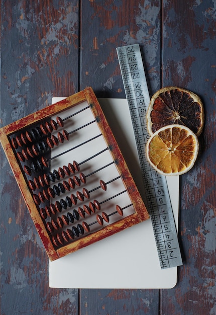 Photo vintage abacus with notebook pen and dried orange slices on rustic wooden table