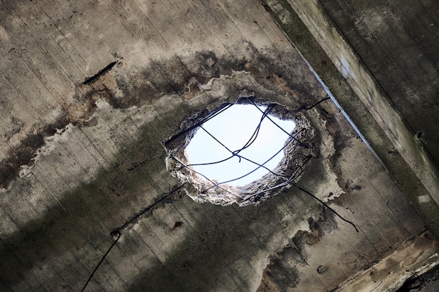 Vintage abandoned damaged house roof with hole in ceiling overlooking cloudy sky. Collapsed concrete wall with hole in abandoned industrial or residential building, close up