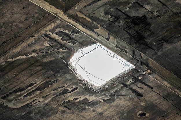 Vintage abandoned damaged house roof with hole in ceiling\
overlooking cloudy sky. collapsed concrete wall with hole in\
abandoned industrial or residential building, close up