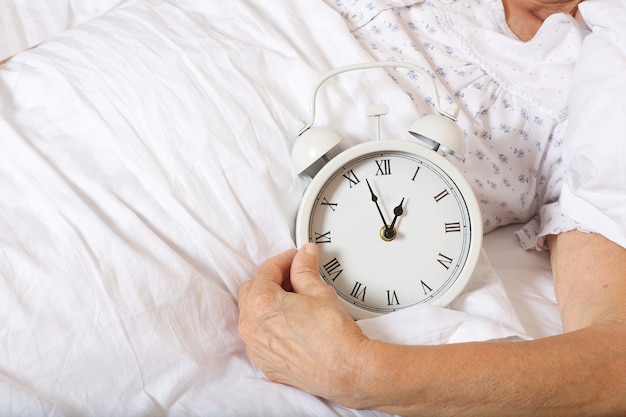 Vintage alarm clock on the bed of senior woman