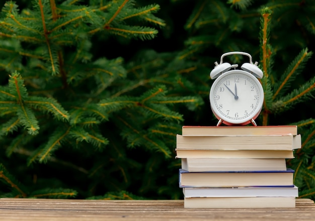 Vintage alarm clock and books on wooden table with spruce branches on background