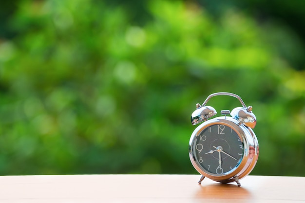 Vintage alarm clock on green burred background.