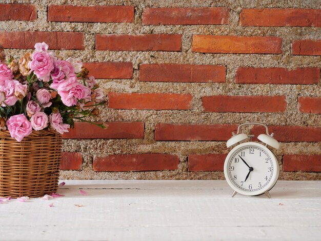 Vintage alarm clock with roses in basket on white wooden table