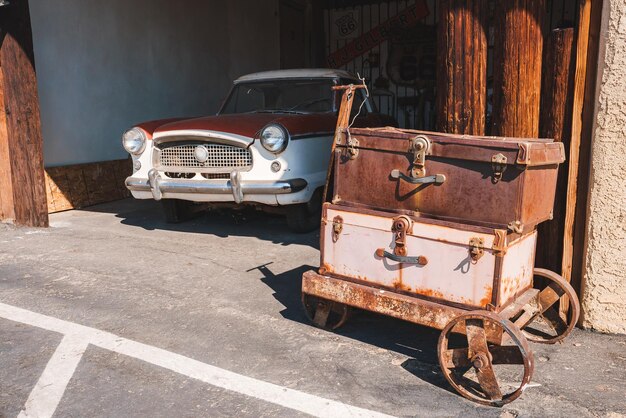 写真 ヴィンテージ・アメリカナ・シーン (vintage americana scene)  腐った荷物カートとクラシックカーバーストー・usa (barstow usa)