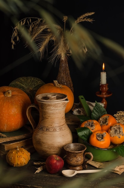 Vintage autumn still life with pumpkins persimmons and wheat grain ears on an old wooden surface on a black background