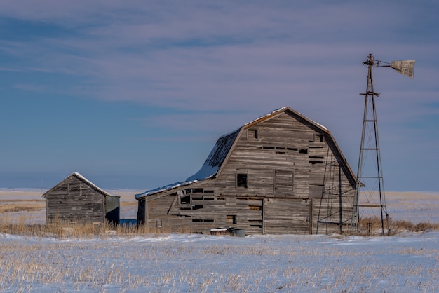 Granaio d'annata, recipienti e mulino a vento circondati da neve sotto un cielo rosa di tramonto in saskatchewan, canada