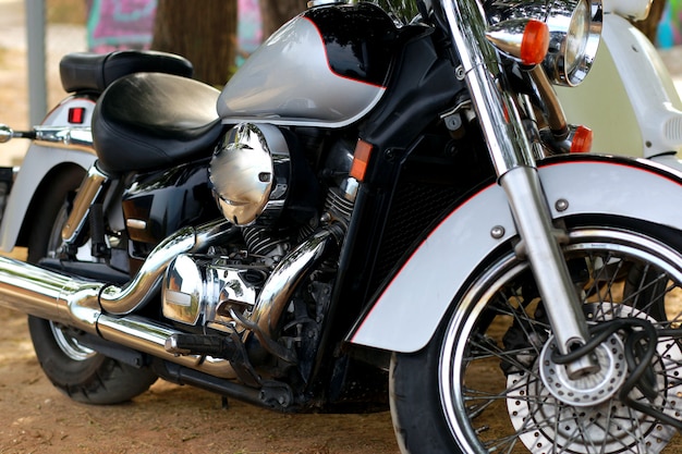 日光の光線で白いバイク近くに立っているヴィンテージの黒いオートバイ。側面図