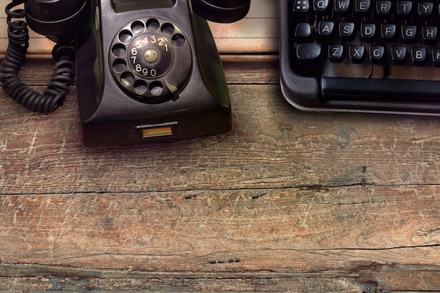 Vintage black phone and typewriter on wooden table background