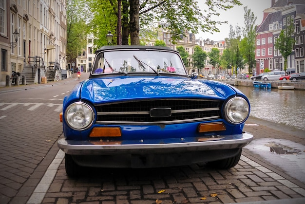 Photo vintage blue car is parked on the street along a canal in amsterdam, netherlands