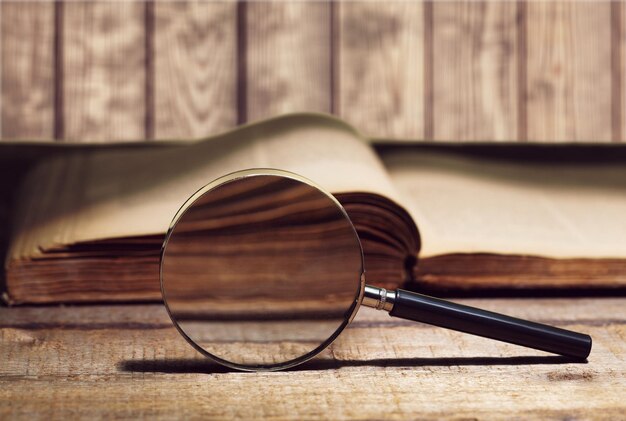 Vintage book and magnifying glass on wooden background