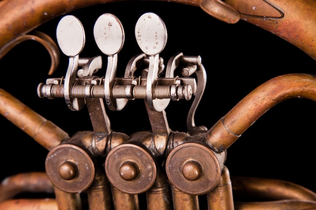 Vintage bronze pipes, valve, key mechanical elements french horn on black isolated background.