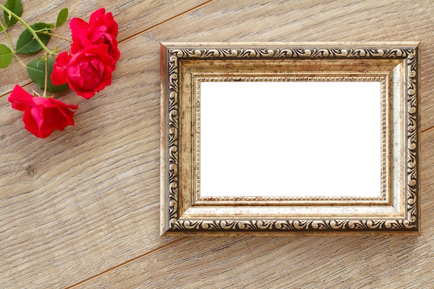 Vintage brown photo frame with copy space and red rose flowers on wooden boards. Top view.