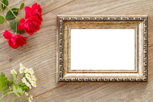 Vintage brown photo frame with copy space red rose and white chamomile flowers on wooden boards