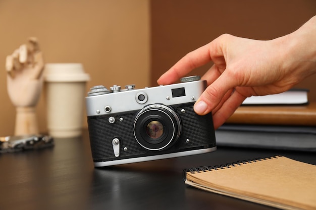 Vintage camera in female hand and notepad on wooden table on brown background