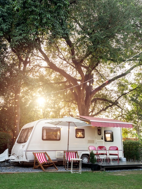 Vintage caravan car parking in garden decoration with empty seats and table on big tree background vertical style Relax camping and sleep in the motorhome trailer Family vacation travel concept