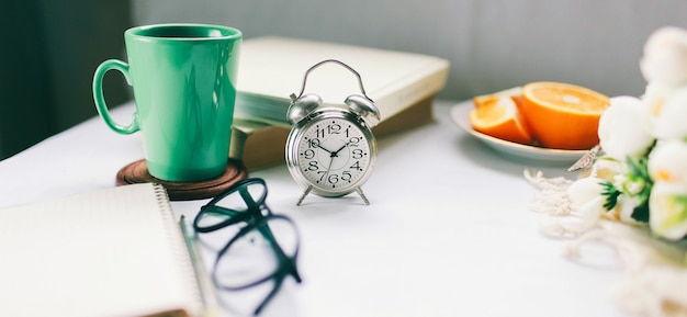 Orologio vintage su una scrivania con una tazza di caffè caldo e frutta fresca