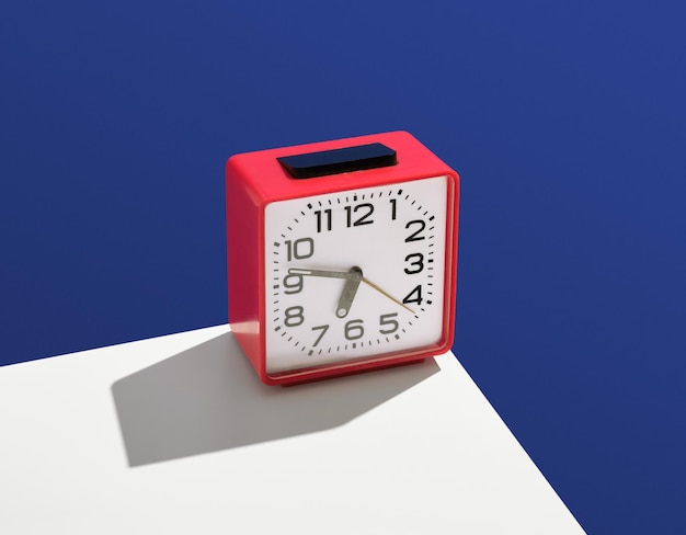 Vintage clock square shape and red color stand on white table. Idea of work, punctuality and expectation. Minimalistic retro composition.