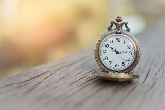 Vintage clock on wooden table with nature background.