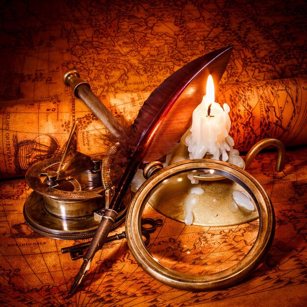 Vintage compass, magnifying glass, pocket watch, quill pen, spyglass lie on an old ancient map in 1565 with a lit candle. Vintage still life.