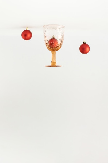 Vintage drinking glass and red Christmas baubles decor turned upside down on white background
