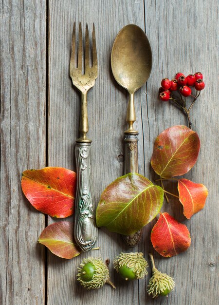 Vintage fork and knife with autumn leaves on wood on wooden table top view