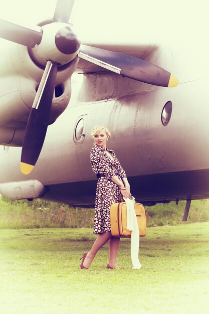 Vintage gestileerde foto van mooi meisje met gele koffer en vliegtuig op background