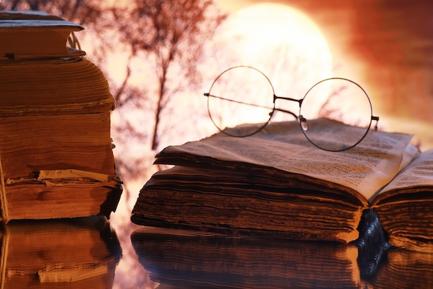 Винтажные очки на старой ретро-книге на фоне луны. Чтение книги при свечах. Концепция книжных триллеров и романов.