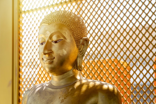 Vintage gold buddha statue in front of yellow orange grill\
background with the square pattern light from behind