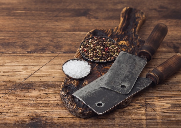 Vintage hatchets for meat on wooden chopping board with salt and pepper on wooden background.