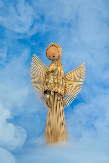 Foto vintage houten stro reed engel engel pop tegen blauwe achtergrond met mistige rook