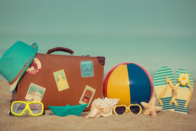 Vintage koffer en slippers op zandstrand tegen blauwe zee en lucht