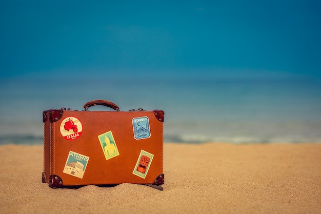 Vintage koffer op zandstrand tegen blauwe zee en lucht zomervakantie en reisconcept