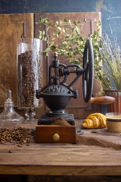 Vintage koffiemolen koffie en croissant op een donkere achtergrond