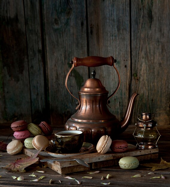 Vintage koperen koffiepot, kopje zwarte koffie en kleurrijke bitterkoekjes op rustieke houten achtergrond.