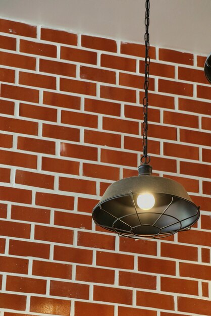 Vintage lamp hanging from the ceiling with light on the brick wall.