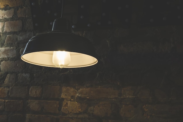 Винтажная лампа с лампочкой, висящей на стене из красного кирпича в темноте