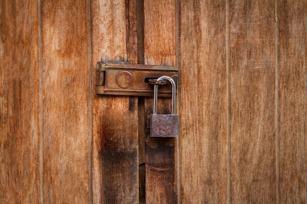 Vintage locked padlock with chain at brown wooden door background, Closeup