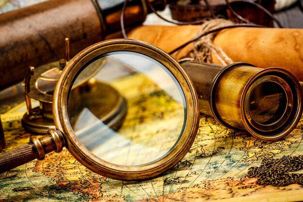 Vintage magnifying glass, compass, telescope and a pocket watch lying on an old map.