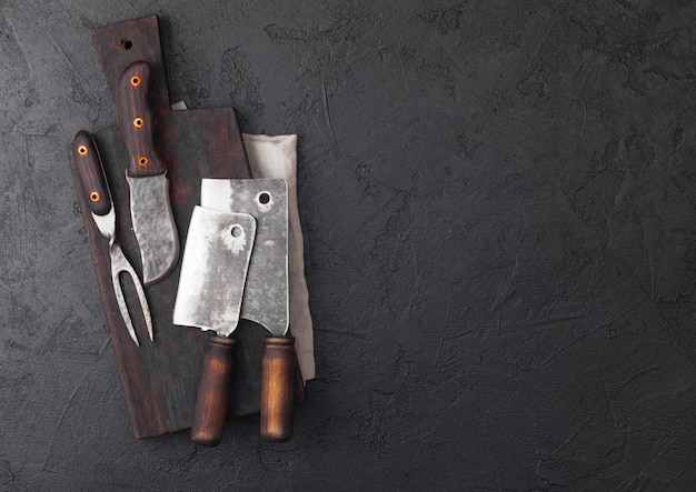 Vintage meat knife and fork and hatchets with vintage chopping board and black table.