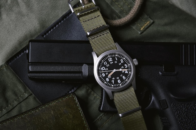 Vintage militaire horloge portemonnee en pistool op legergroene achtergrond, klassiek uurwerk mechanisch polshorloge, militaire mannen mode en accessoires.