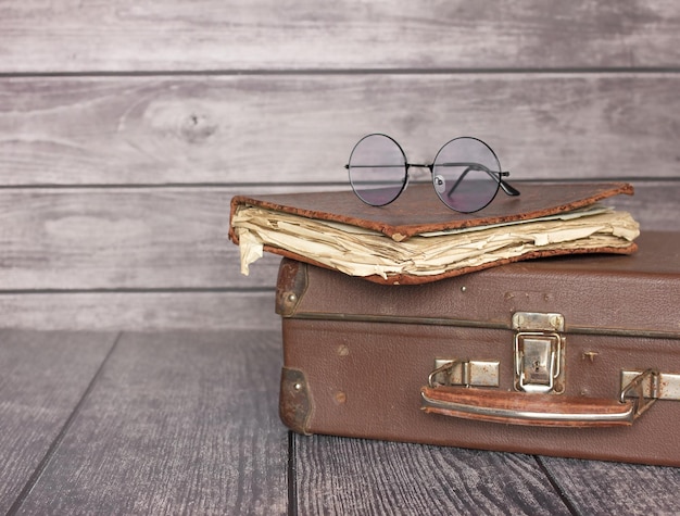 Vintage old classic 1950s style leather travel suitcase with retro book and round glasses. Travel luggage concept. copy space